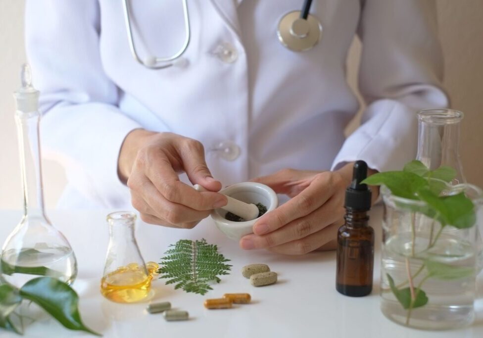 Doctor preparing herbal medicine with plants and tools.